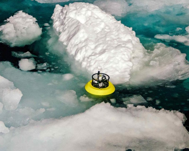 A device in the water, amid pieces of sea ice, measures underwater warm areas.