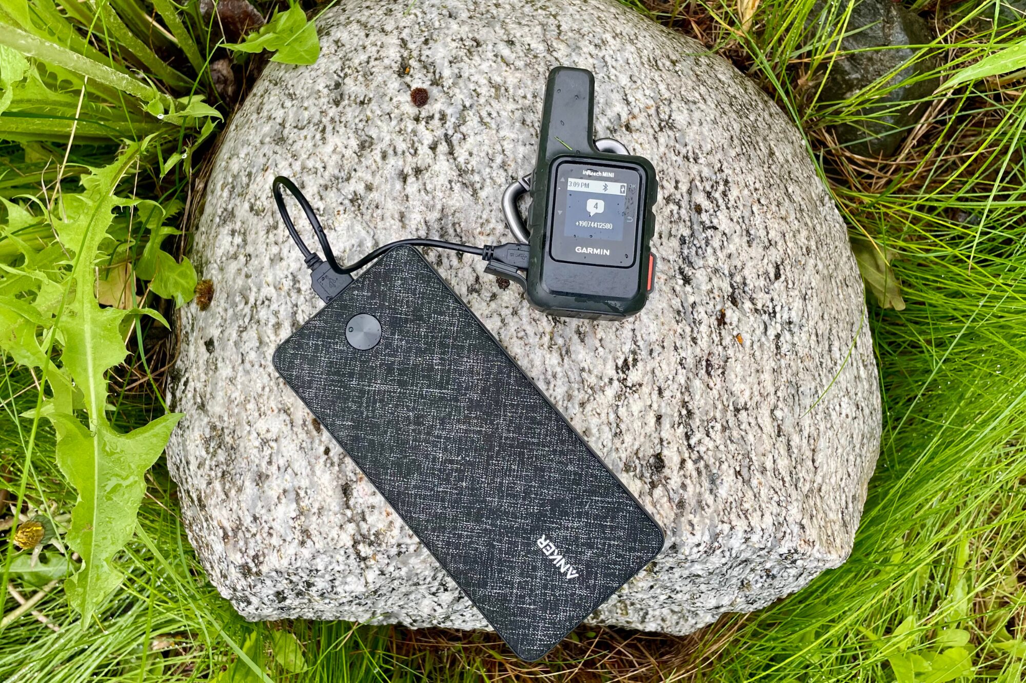 An Anker power bank charges an inReach device, while sitting on a stone. 