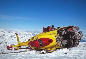 A yellow-and-red helicopter destroyed and layin on the snow on one side.