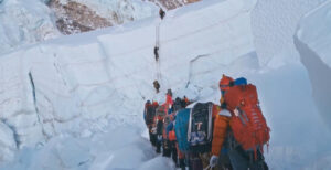 Climbers in line in front of a big seraac with a ladder on it.