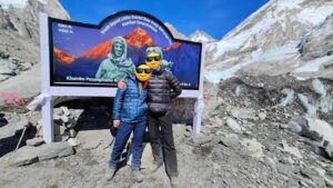 two climbers with faces hidden with emojis pose in front of the billboard at Everest Base Camp.