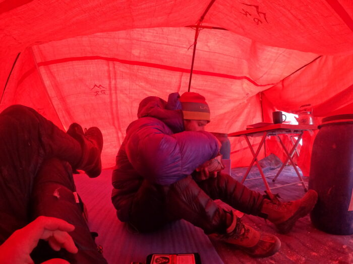 A climber sitting on the ground in a tent. 