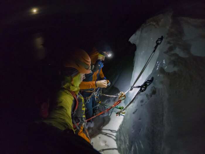 the climbers at an ice belay in pitch black darkness, the moon in background. 