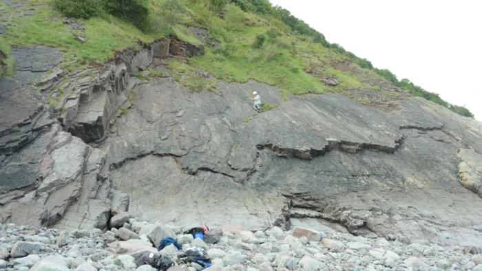 man exploring a cliff in white clothing with gear at the base