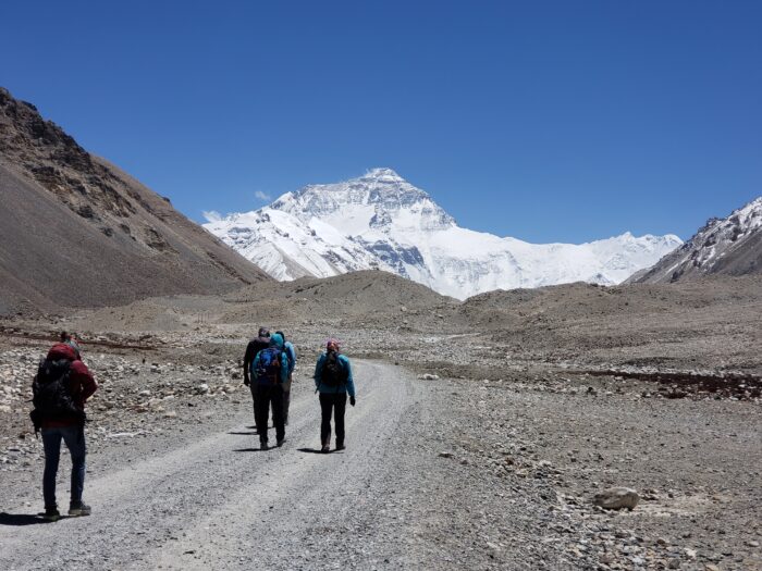 Climbers on a dirt road on a plain with the north side of Everest in background.