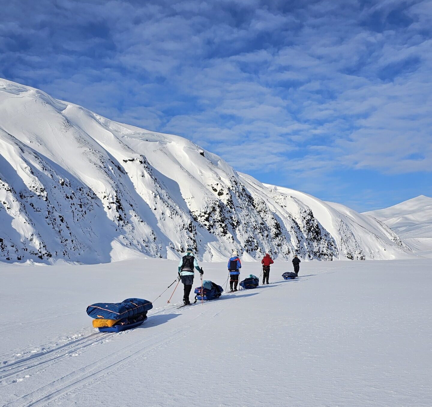 Line of polar skiers beside white mountain