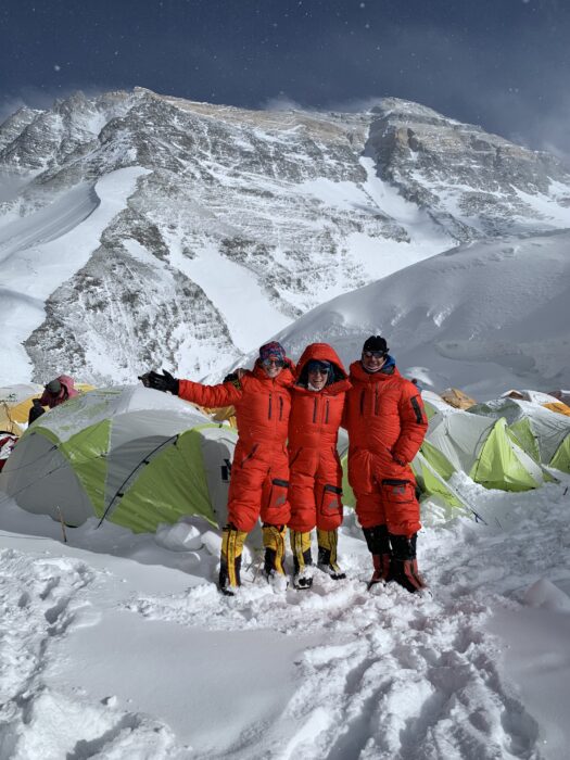 The climbers in front of some tents and a snowy Everest behind.