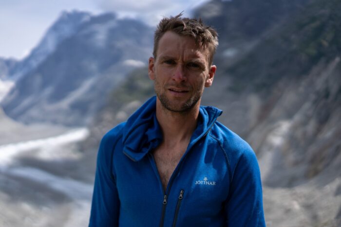 Close shot of Howell in a blue fleece, mountains and a glacier behind. 