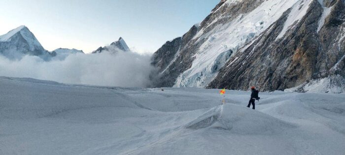 A climber on a flat area on Everest, with a serac covered slope to the right and clouds covering the glacier below. 
