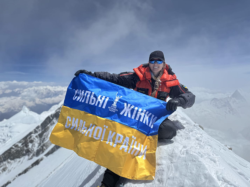 Irina on the snowy, narrow summit of Annapurna, holds an Ukrainian flag