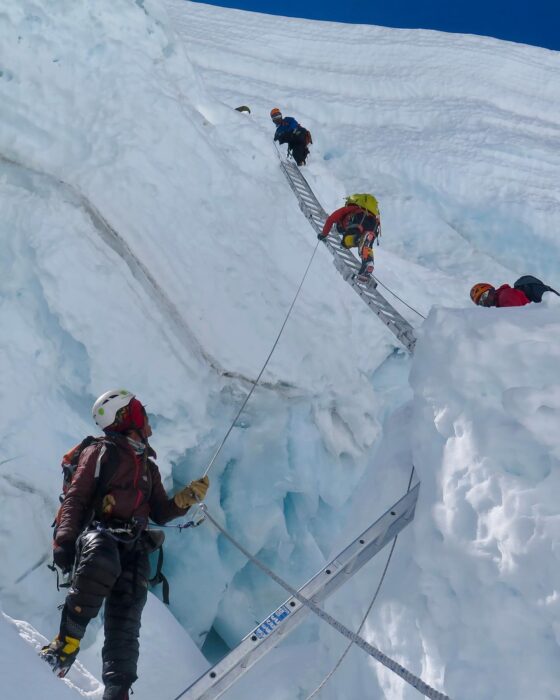 A Sherpa belaying clients as they proceed up a ladder on Everest's Khumbu Icefall