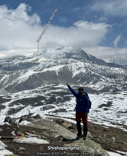 A climber points to a peak in the distance, marked as Shishapangma 