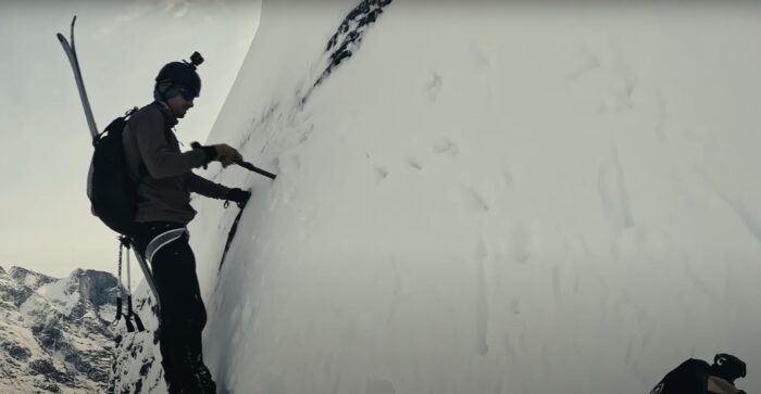 a man climbs a vertical face with skis on his back