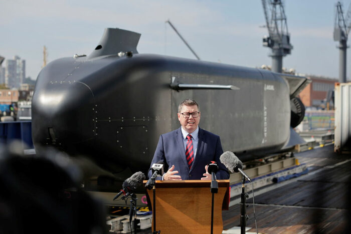 Suited man speaking in front of a submarine-shaped UUV