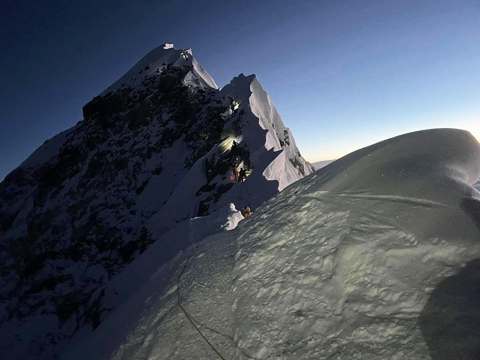 a few climbers with headlamps on the summit of Everest at sunrise