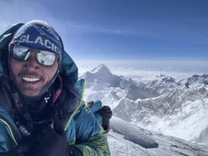 Sherpa smiling on the summit of Everest with Makalu behind him