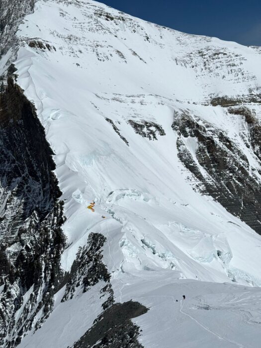 a single climber on a huge snow slope with Camp 3 tents in the middle