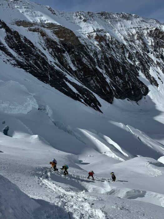 four climbers progress on fresh snow with the huge north face of Everest behind them. 