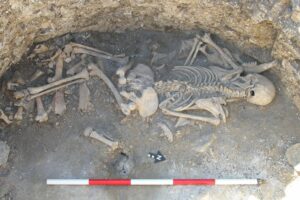 complete but battered skeleton lying on dirt in a pit