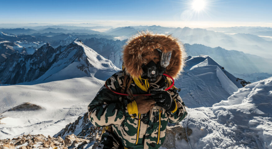The Sherpa wears supplementary Oxygen on the summit of Makalu, mountains in background.