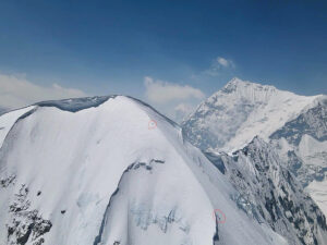 Climbers seem tiny as they progress up the snowy ridge.