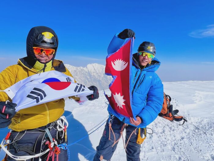 The climbers on a flat, snowy summit holding national flags. 