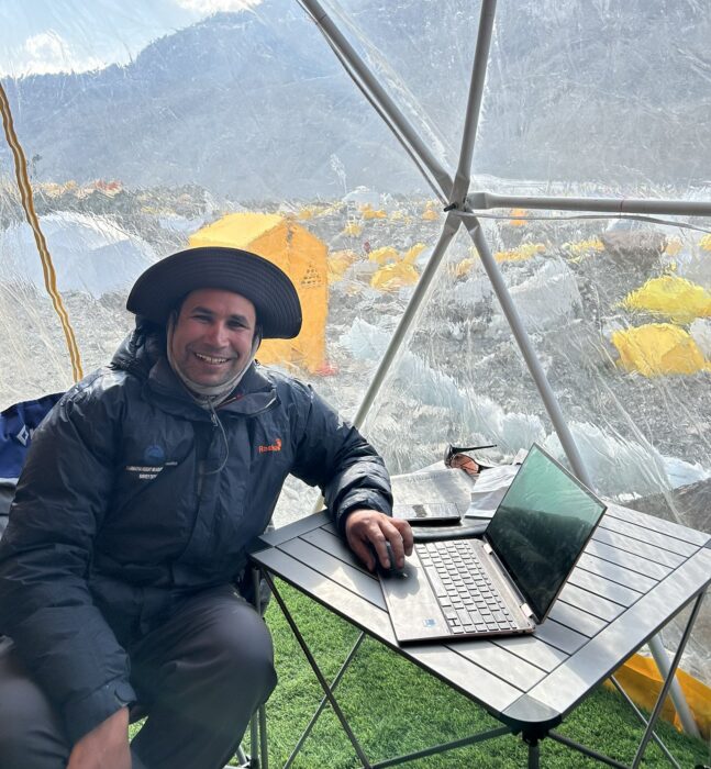 Gautam works with a laptop in front of the transparent side of a tent in Everest Base Camp
