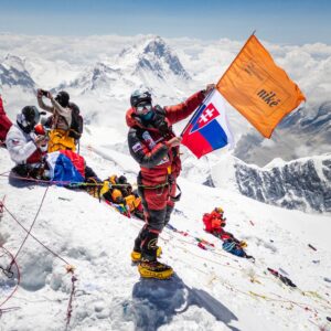 Polackova holds some flags on the summit of Everest in a sunny day, Makalu in background