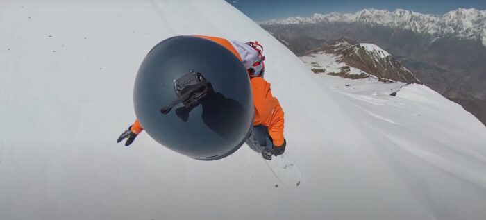 a helmet cam POV shot of a snowboarder with mountains in the background