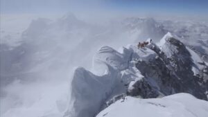 Climbers on a snow-loaded summit ride on Everest, in clouds