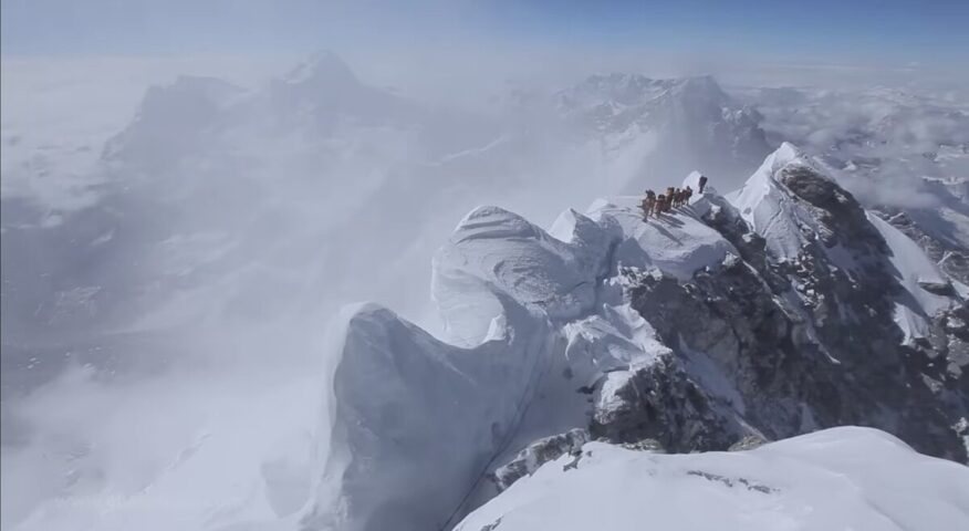 Climbers on a snow-loaded summit ride on Everest, in clouds