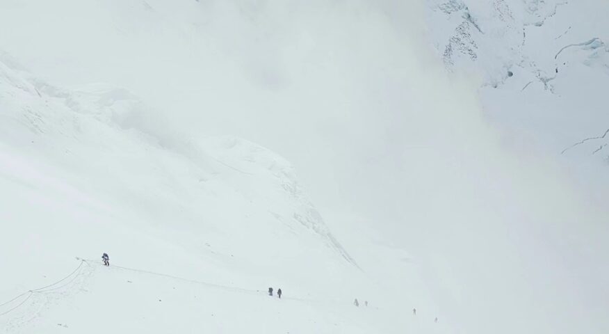 tiny figures of climbers on a huge, while slope on a foggy day on Everest as they climb the Lhotse Face