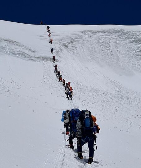 Climbers cliped to a rope in a long line up a serac on Kangchenjunga