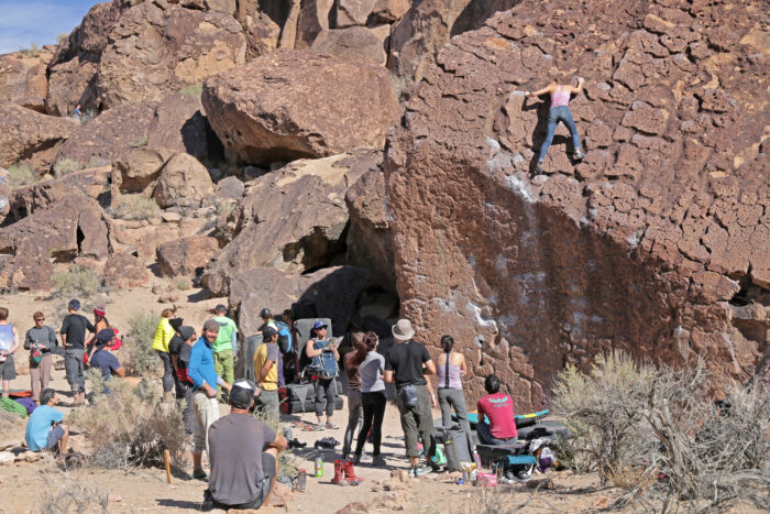 people crowded around a boulder with a climber nearing the top