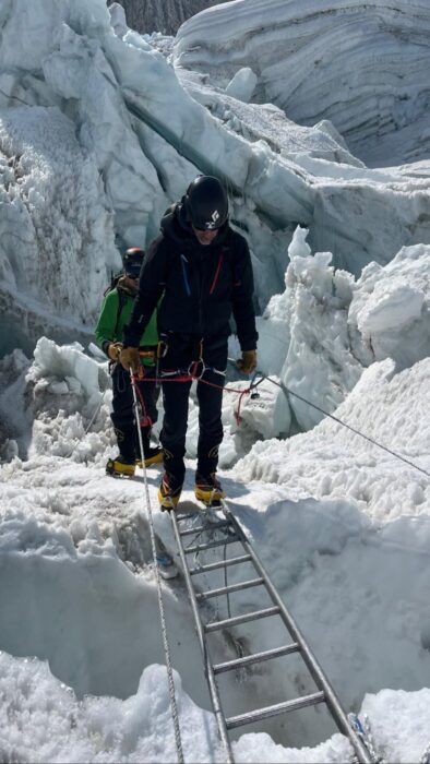 cimbers on a ladder, crossing a crevasse at the khumbu icefall on Everest