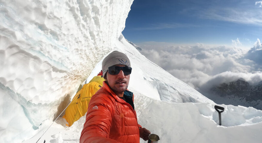 sajid takes a selfie under a serac, with a sea of clouds behind him.