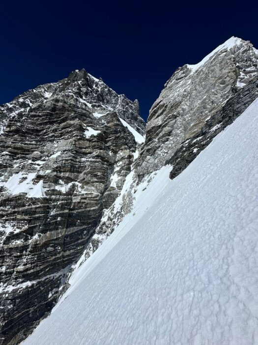 A rockly face split in two by a dihedral and a thin couloir heading to the higher peak