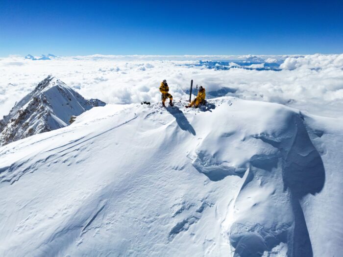 The climbers on a snowy summit, a pair of skis stuck on the snow. 