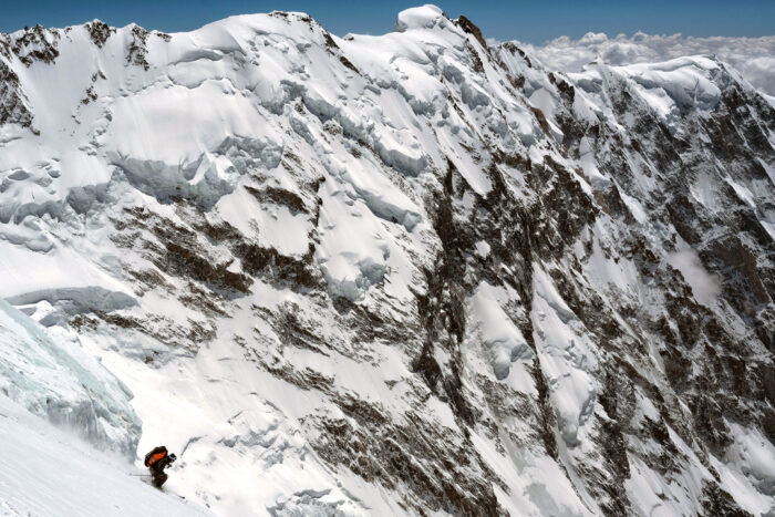 The skier down a steep ramp on a huge moutnain face.