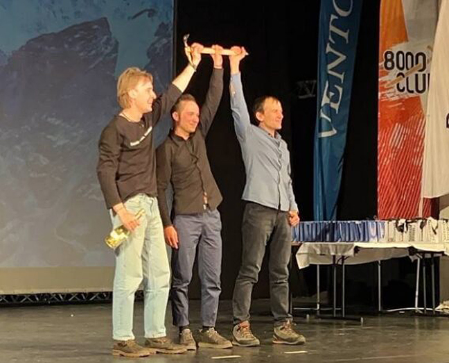 three men on stage raise ceremonial ice ax