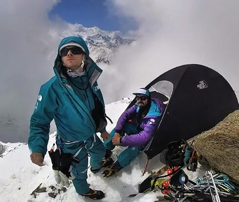 Goettler looks up and Arnold sits by the tent's gate on a snowy mountain camp