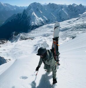 the climber on deep snow, leans on an iceaxe and carries skis on his backpack.