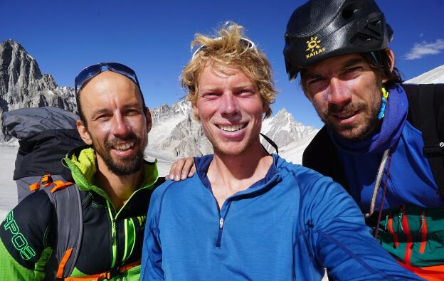 the climbers pose for a selfie smiling, with moutains behind