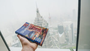 a hand holds a book in front of a window with skyscrapers in the background