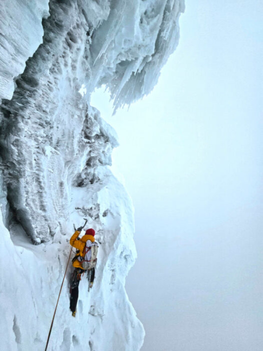 A climber traversing under an overhanging ice serac on Pisco, Andes