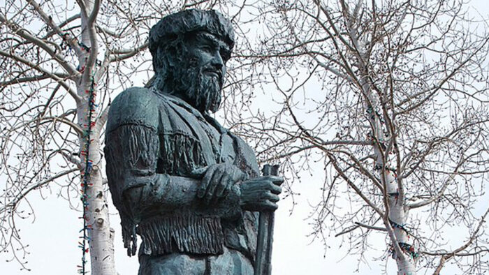 a statue of Old Bill Williams with trees in the background