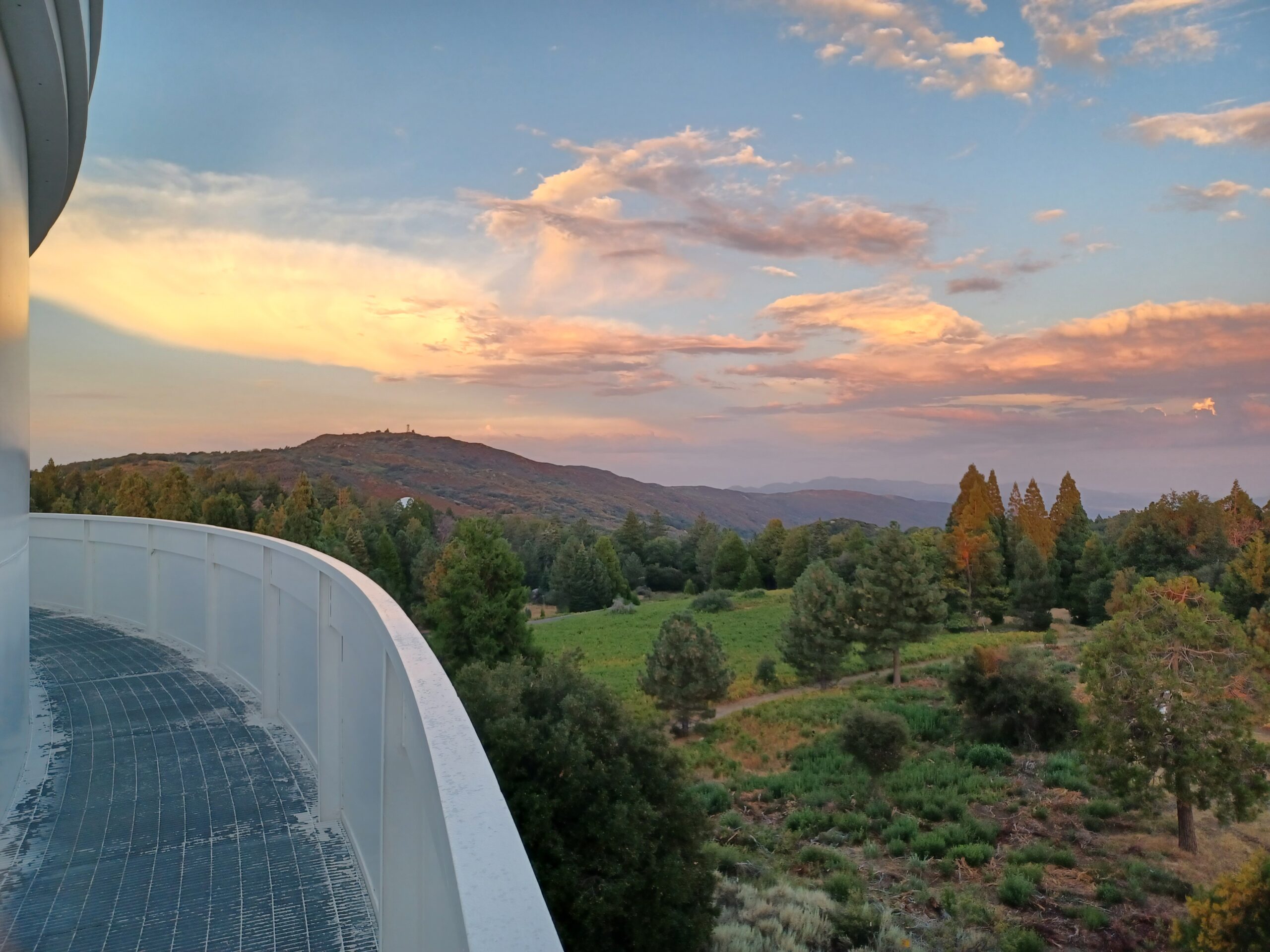 Photo taken of a sunset over rolling hills from a metal catwalk.