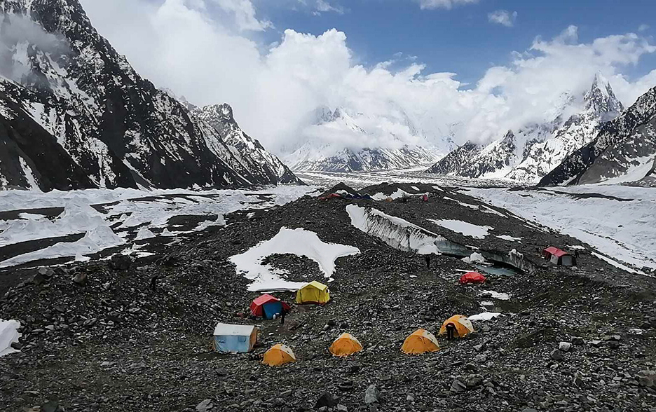 A few tents on a flat, rocky glacier and Broad Peak's flanks on the left