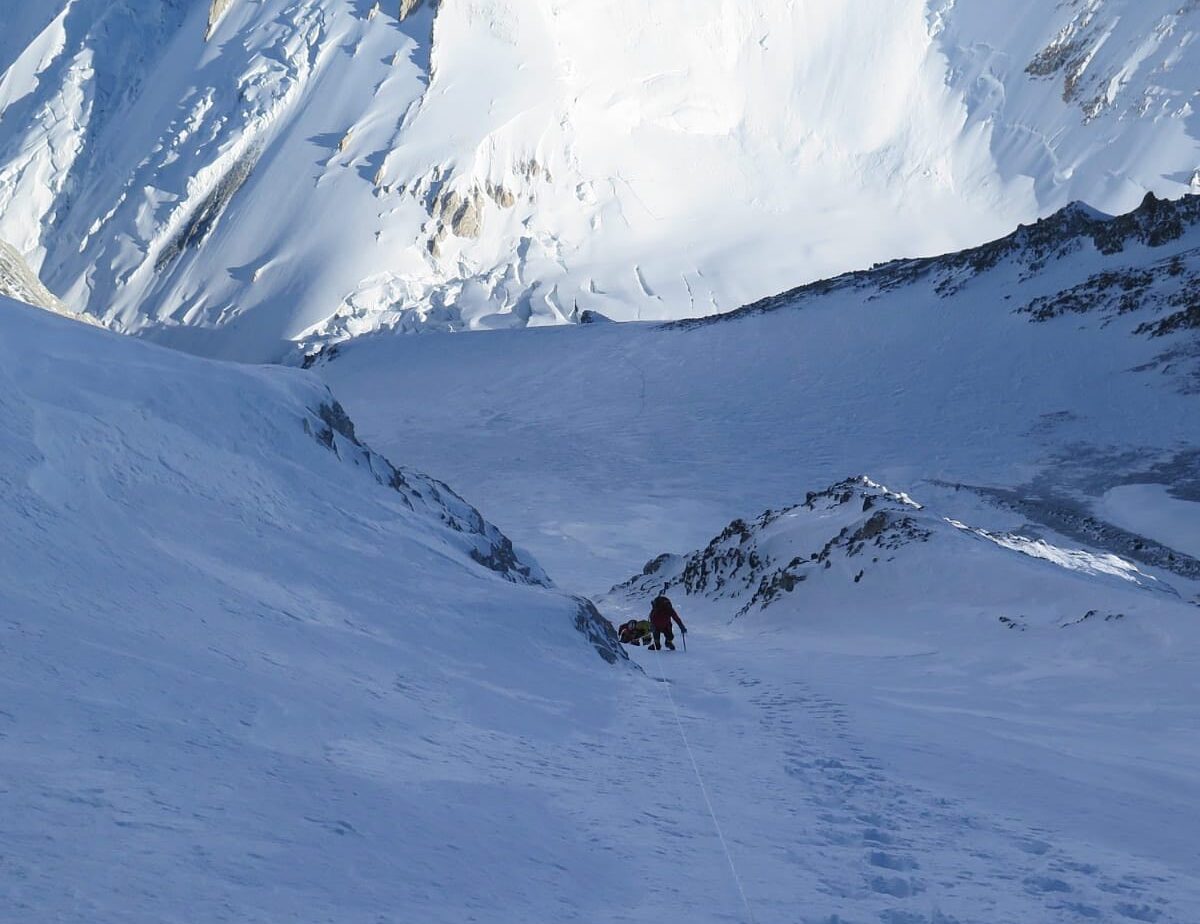 Climbers on a snow slope in the shade, the opposite peak in the sun behind them.