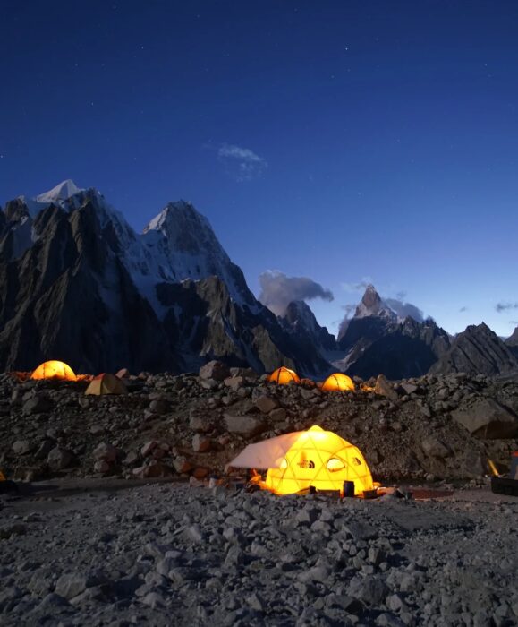 a Base Camp illuminated in the last lights of the day, with an impressive background of jagged peaks. 